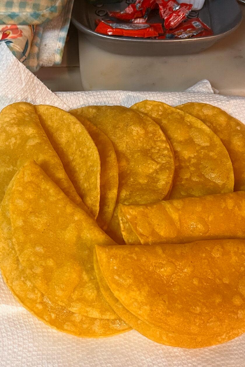 Folded corn tortillas just fried in oil drain on paper towels.