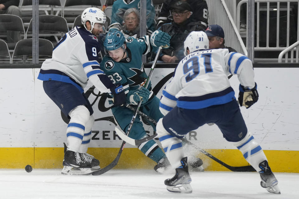 San Jose Sharks defenseman Calen Addison (33) skates toward the puck from between Winnipeg Jets left wing Alex Iafallo (9) and center Cole Perfetti (91) during the second period of an NHL hockey game in San Jose, Calif., Thursday, Jan. 4, 2024. (AP Photo/Jeff Chiu)