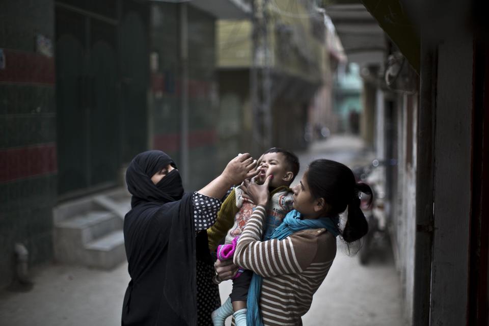 A Pakistani woman, right, holds her nephew to be vaccinated against polio by Mariam Jabir, 32, while going house to house checking on children who need the vaccine, in Rawalpindi, Pakistan, Tuesday, Jan. 21, 2014. Gunmen in a pair of attacks minutes apart struck two teams of polio workers in the southern city of Karachi, killing three members of the teams and wounding a fourth before fleeing, police said. Police official Pir Mohammad Shah said two female and a male worker were killed in the attacks in Karachi, the capital of southern Sindh province.(AP Photo/Muhammed Muheisen)