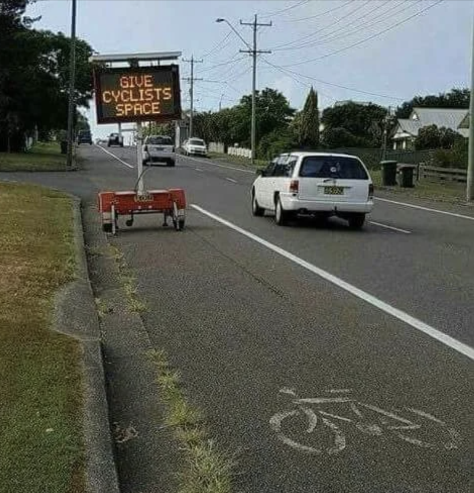 Electronic roadside sign reads "GIVE CYCLISTS SPACE" next to a bike lane with a car approaching