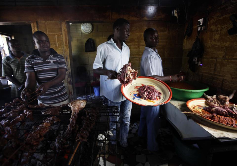 In this photo taken on Saturday, Oct. 20, 2012, men grill meat into suya in Lagos, Nigeria. As night falls across Nigeria, men fan the flames of charcoal grills by candlelight or under naked light bulbs, the smoke rising in the air with the smell of spices and cooking meat. Despite the sometimes intense diversity of faith and ethnicity in this nation of 160 million people, that thinly sliced meat called suya, is eaten everywhere. (AP Photo/Sunday Alamba)