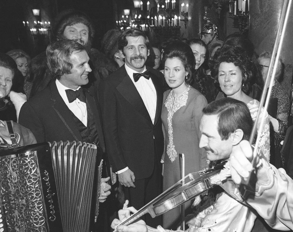 FILE - Norman Jewison, left, Israeli actor Chaim Topol, center, and his wife listen to violinist Pali Gesztros at a gala at the Paris Opera for the benefit of Jewish charity organizations and the film "Fiddler on the Roof" in Paris on Dec. 1, 1971. Topol, a leading Israeli actor who charmed generations of theatergoers and movie-watchers with his portrayal of Tevye, the long-suffering and charismatic milkman in “Fiddler on the Roof,” has died in Tel Aviv, Israeli leaders said Thursday, March 9, 2023. He was 87. (AP Photo, File)