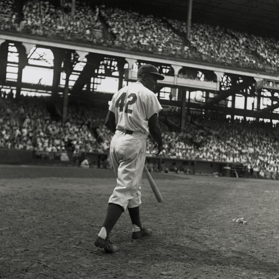 A Black baseball player wearing the number 42 steps up to bat in a stadium packed with thousands of fans.