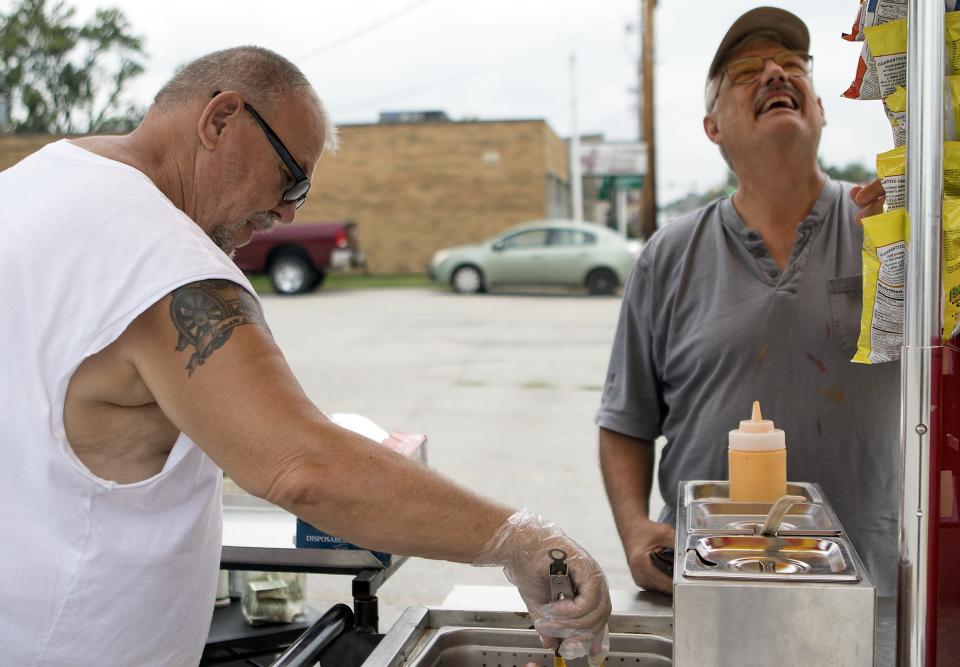 Grandpa's Hot Dog Cart owner Junior Bledsoe prepares a hot dog as customer Glenn Busse, right, looks over the selection of potato chips.