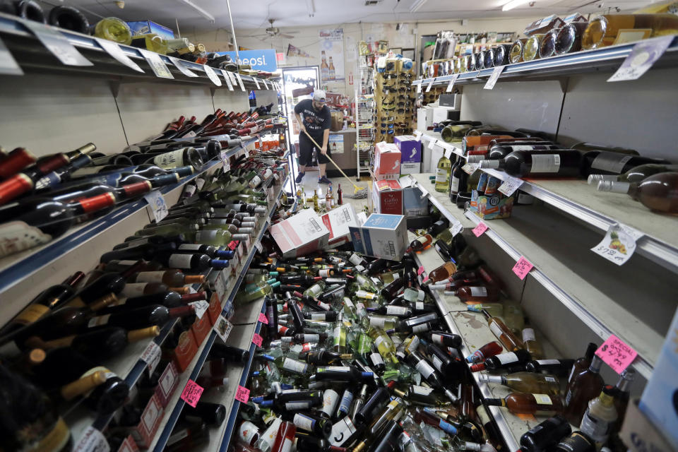 FILE - In this July 6, 2019, file photo, bottles of wine are strewn in the middle of an aisle as Victor Abdullatif, background center, mops inside of the Eastridge Market, his family's store, in Ridgecrest, Calif., following the largest earthquake the region has seen in nearly 20 years jolted an area from Sacramento to Las Vegas to Mexico. The virus outbreak is compromising the ability of nations to prepare for natural disasters and deal with the aftermath. Every year, the world contends with devastating typhoons, wildfires, tsunamis and earthquakes. (AP Photo/Marcio Jose Sanchez, File)