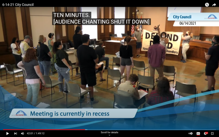 In this image captured from a City of Des Moines video, Paden Sheumaker can be seen leading protest chants in front of a &quot;Defund DMPD&quot; banner during the June 14 meeting of the City Council.