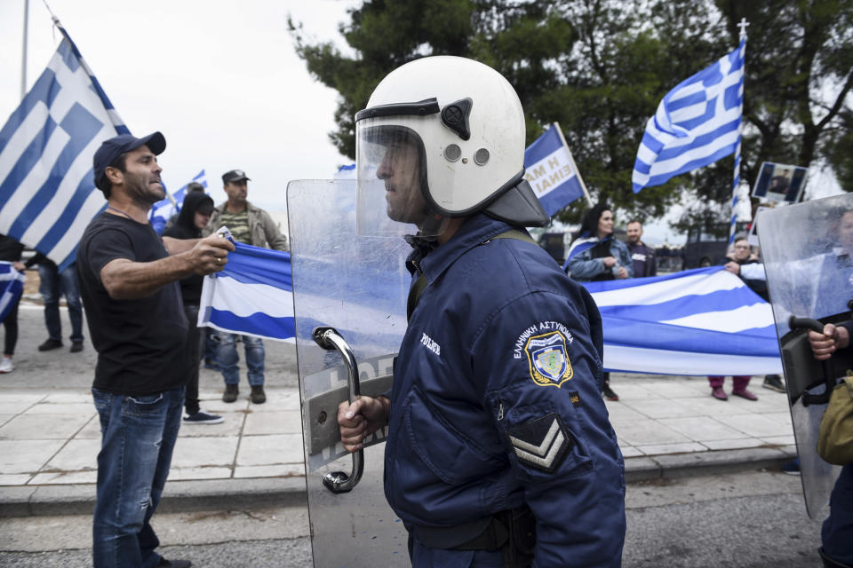 A Greek policeman walks in front of protesters opposing Greece's name deal with neighboring Macedonia, near Evzonoi border crossing in Greece, Sunday, Sept. 30, 2018. Macedonians were deciding on their country's future Sunday, voting whether to accept a landmark deal ending a decades-long dispute with neighboring Greece by changing their country's name to North Macedonia. (AP Photo/Giannis Papanikos)