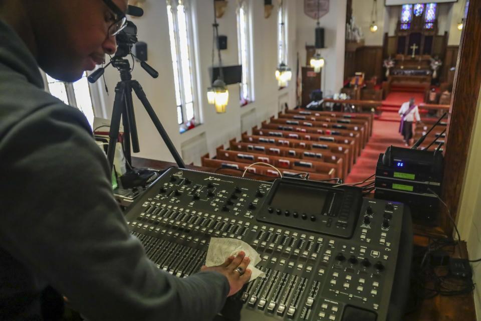 Multimedia technician Joseph Stoute, 21, use a disinfectant wipe to clean the audio equipment at St. Paul's Methodist Church in Brooklyn, New York, where he directed a livestream online broadcast Sunday for homebound congregants due to citywide restrictions aimed at controlling the COVID-19 outbreak. (AP Photo/Bebeto Matthews)