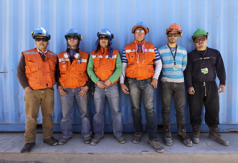 In this Sept. 25, 2012 photo, workers from the National Copper Mine Corporation, or Codelco, pose for a portrait as they wait for a bus home after a work day at the Chuquicamata copper mine in the Atacama desert in northern Chile. Experts say that by 2019 the Chuquicamata copper mine will be unprofitable, so state-owned mining company Codelco is trying to head off closure by converting the open pit into the world's largest underground mine. Codelco believes the mine still has much more to give, with reserves equal to about 60 percent of all the copper exploited in the mine's history still buried deep beneath the crater. (AP Photo/Jorge Saenz)