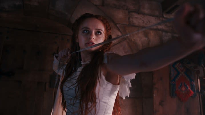 Joey King stands in the shadows, holding a sword, in a scene from The Princess.