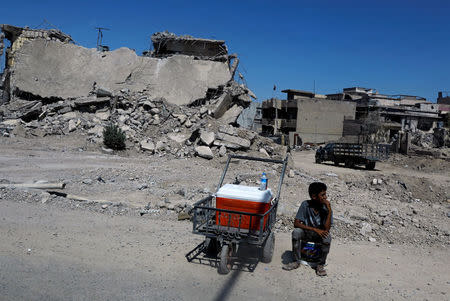 An Iraqi boy sells water in front of destroyed houses on a street in Western Mosul, Iraq August 7, 2017. Picture taken through a glass window. REUTERS/Suhaib Salem