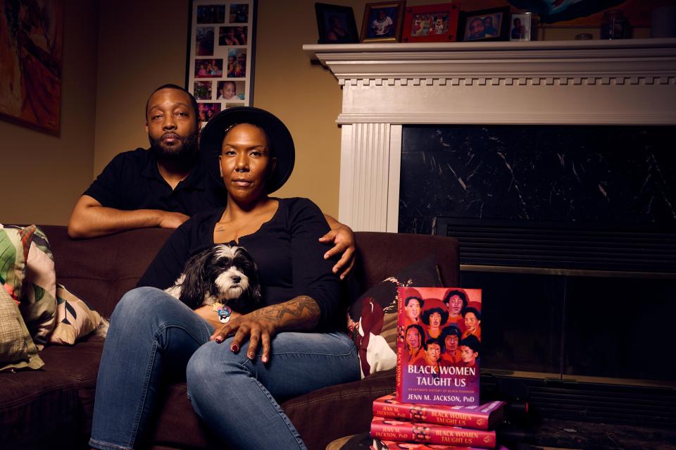 Couple sitting on a couch with a dog and a stack of books including "Black Women Taught Us" by Jewell Jackson