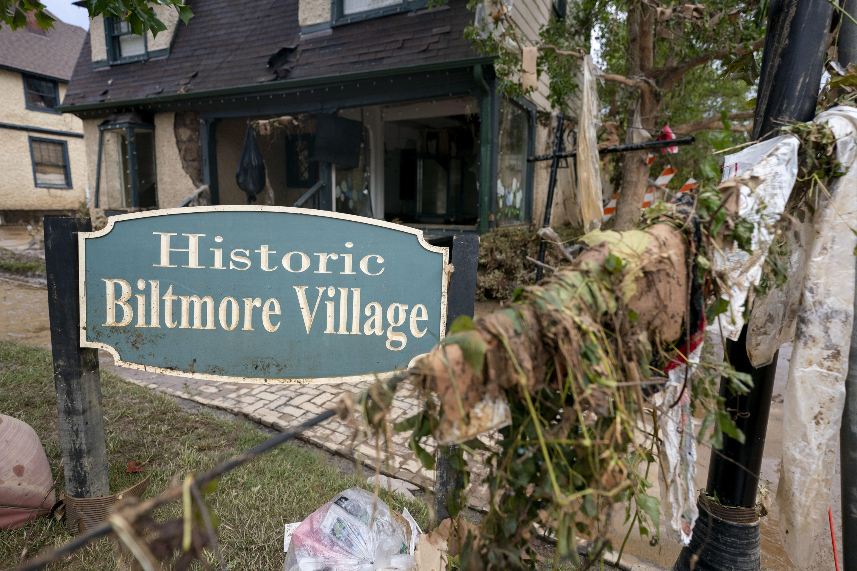 A Biltmore Village sign in front of a damaged building and amid debris. 