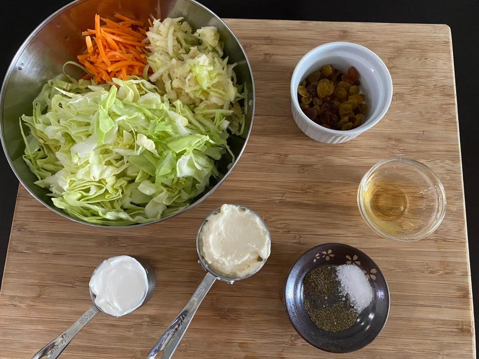 Ingredients for coleslaw in bowls on a wooden cutting board.