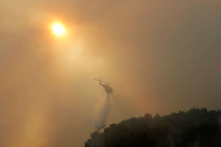 A helicopter drops water as smoke from a burning wildfire fills the sky in Carros, near Nice, France, July 24, 2017. REUTERS/Eric Gaillard