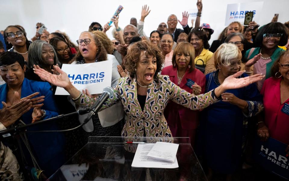 A throng of people supporting Kamal Harris, with Maxine Waters at the front behind a lectern