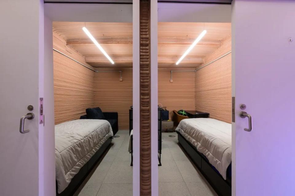 open doors to two identical bedrooms with twin beds, wood slat walls, and one strip overhead led light