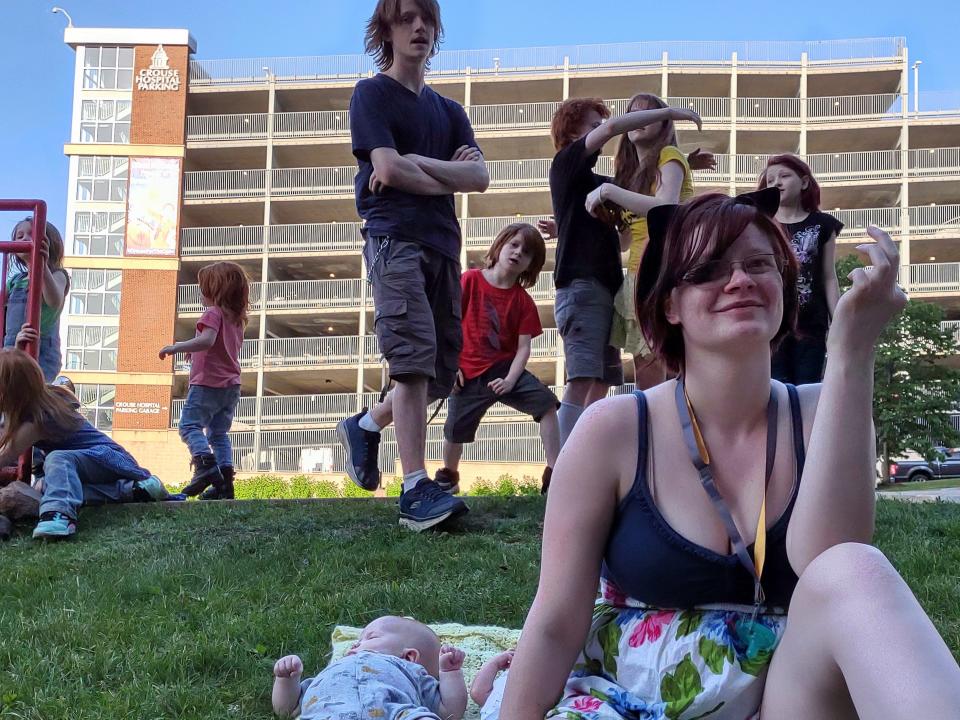 Victoria Merritt, the oldest child of TikTok's mom-of-12, Veronica Merritt, poses with her two-month-old sibling, Modi, left and her own one-week old newborn, Maddilyn, while some of Maddilyn's other aunts and uncles goof around behind them.