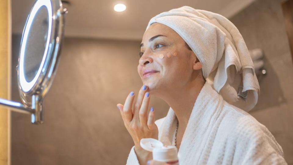 How to get foundation out of clothes: Woman in Bathrobe Applying Cream to Her Face in the Bathroom