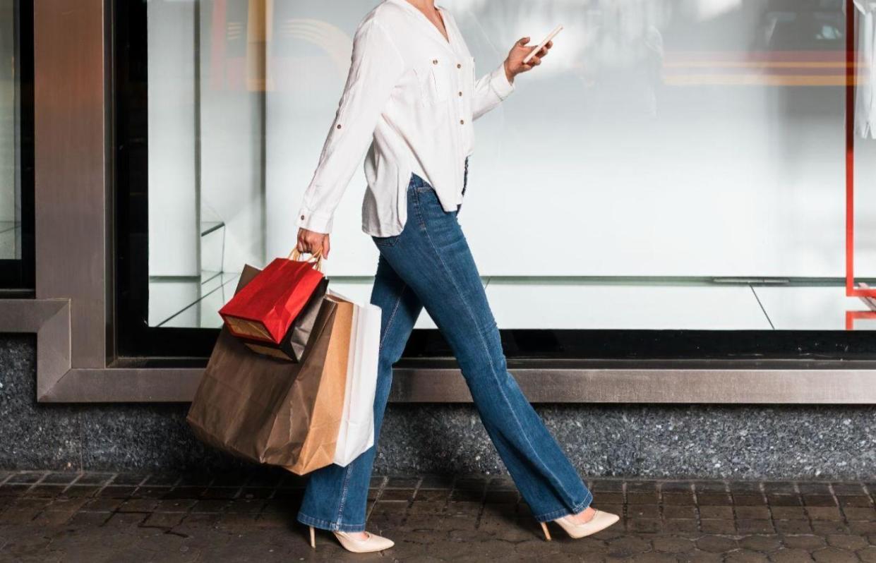 Woman walking on the street and looking at phone while carrying shopping bags. 