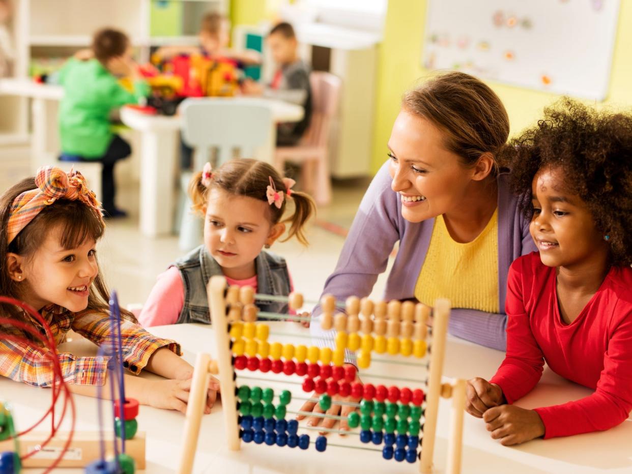 teacher and three girls are sitting around a table and playing with toys at a preschool