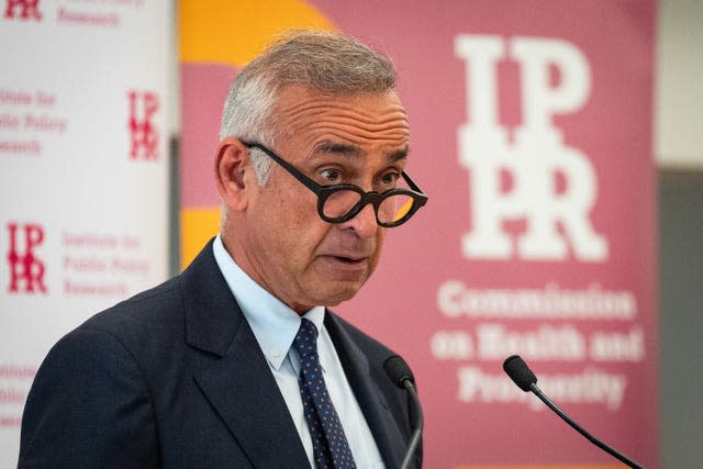 A man peers over the top of thick, black-rimmed glasses as he delivers a speech at a lectern