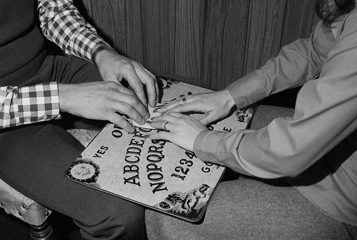 Man and woman with hands on board seek message of spiritualistic or telepathic origin