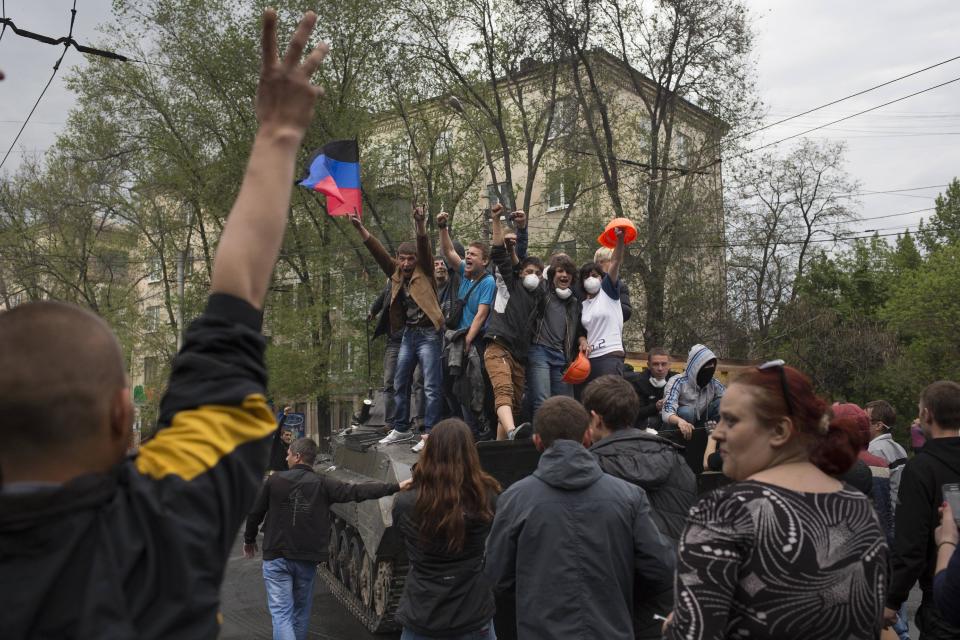 People greet pro-Russian activists atop of a government forces armored personal carrier captured from the enemy in fighting in Mariupol, eastern Ukraine, Friday, May 9, 2014. Fighting exploded Friday in Mariupol, a city of 500,000 on the Sea of Azov that is on the main road between Russia proper and Crimea. The fighting between government forces and insurgents in Mariupol has left several people dead. (AP Photo / Alexander Zemlianichenko)