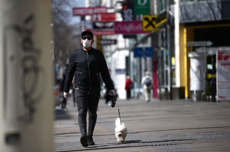 A man wearing a protective mask walks a dog on a shopping street during the global coronavirus disease (COVID-19) outbreak in Vienna
