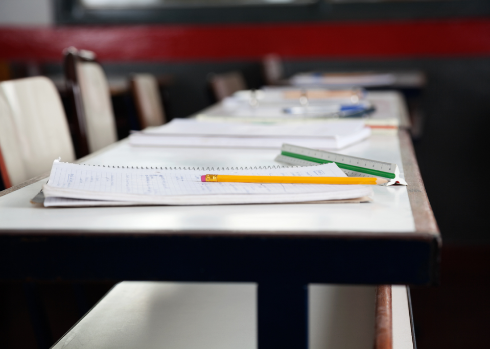 A row of empty desks with notebooks and pencils on them.