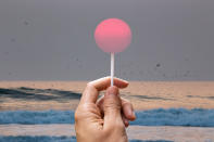 Creative picture of guy holding lollipop stick in the sky matching the setting sun on a California beach.