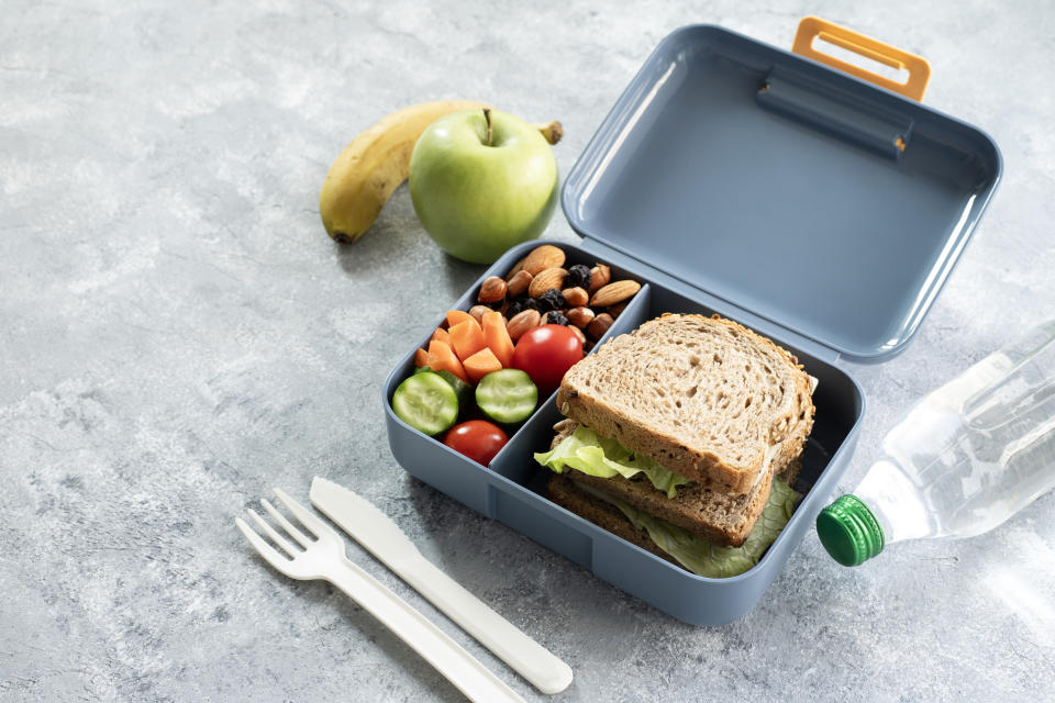 School lunch box with sandwich, vegetables, fruit and water on table, healthy eating concept.