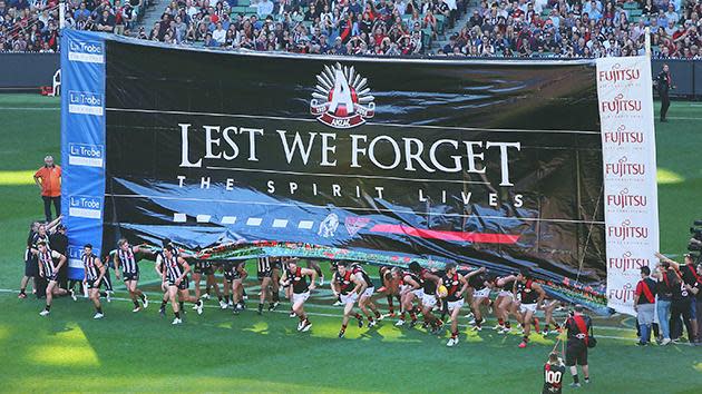 Essendon players run through a commemorative banner.