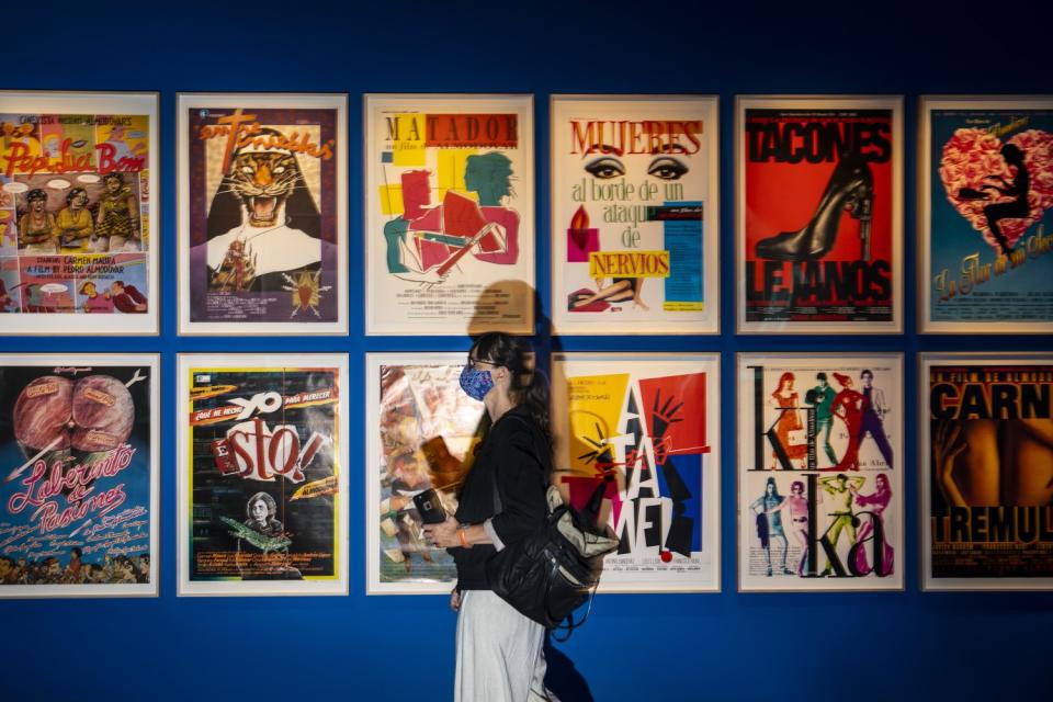 A person wearing a mask walks past a wall covered in posters