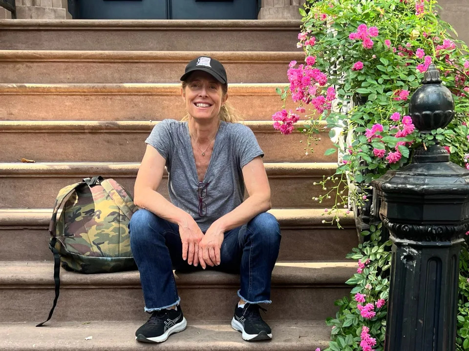 Allison Langer sitting on the steps of a house wearing jeans and a t-shirt and smiling.