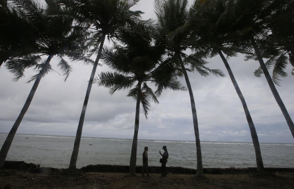 People stand on the shore near the recent tsunami near Carita beach, Indonesia, Friday, Dec. 28, 2018. Indonesia raised the danger level for an island volcano that triggered a tsunami on the weekend, killing at least 430 people in Sumatra and Java, and widened its no-go zone.(AP Photo/Achmad Ibrahim)