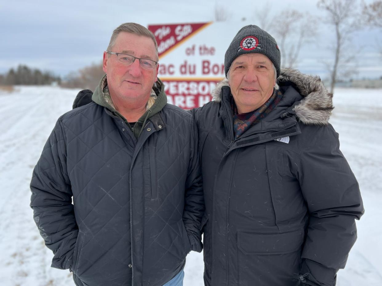 RM of Lac du Bonnet Reeve Loren Schinkel, left, and Town of Lac du Bonnet Mayor Ken Lodge, right, stand next to a sign marking the future site of the community's new personal care home. It was first announced in 2012, but residents are still waiting for construction to start. (Travis Golby/CBC - image credit)