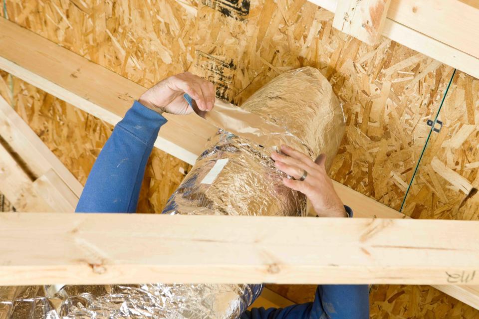 Worker Insulating an Attic Vent Duct with Aluminum Foil Tape