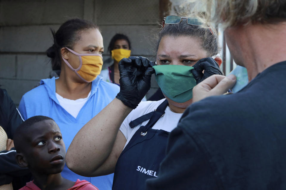 In this May 2, 2020, photo, residents of the Manenberg neighborhood of Cape Town, South Africa, watch as gangs deliver food to the poor and needy during the coronavirus lockdown. A preacher recruited the street gangs and got them to agree to a truce during the deliveries. (AP Photo/Nardus Engelbrecht)