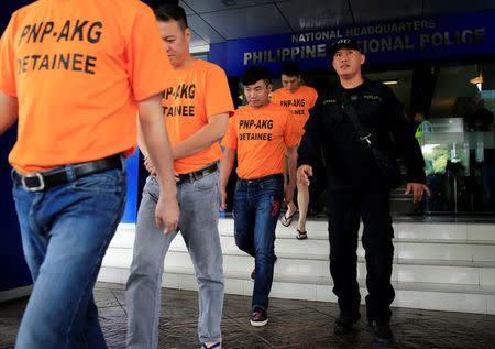 A policeman escorts some of the arrested Chinese nationals involved in kidnapping a Singaporean woman at a casino resort in the capital, during a presentation inside the Philippine National Police (PNP) Headquarters in Quezon City, metro Manila, Philippines July 20, 2017. REUTERS/Romeo Ranoco