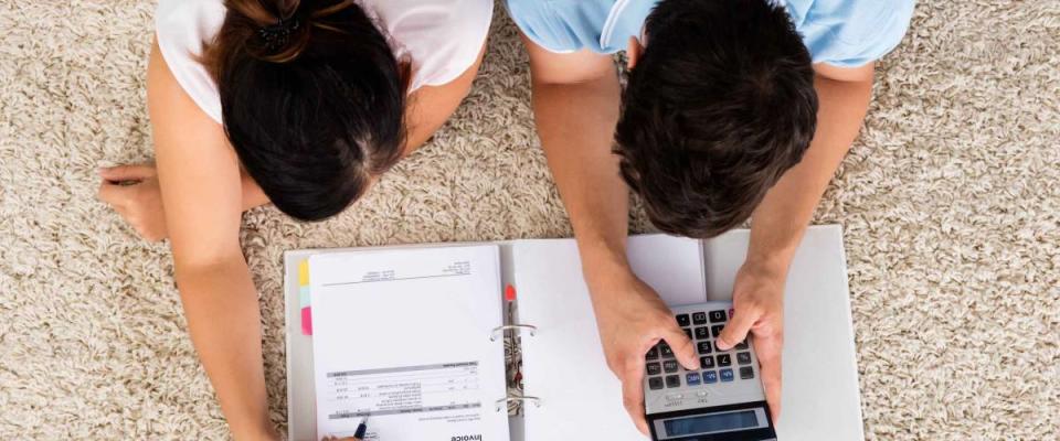 High Angle View Of Couple Calculating Budget Together While Lying On Carpet