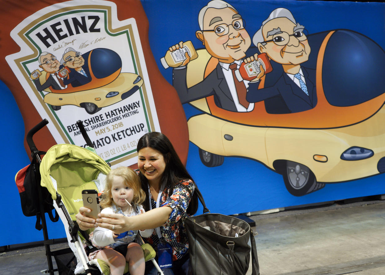 Shareholder Jessica Staben takes a selfie with one-year-old Cecilia Johnson in front of a caricature of Berkshire Hathaway Chairman and CEO Warren Buffett, right, and his Vice-Chairman Charlie Munger, on the exhibit floor at the CenturyLink Center in Omaha, Neb., Friday, May 4, 2018, where Berkshire brands display their products and services. On Saturday, shareholders are expected to fill the CenturyLink arena as they attend the annual Berkshire Hathaway shareholders meeting where Buffett and his Vice Chairman Charlie Munger preside over a Q&A session. (AP Photo/Nati Harnik)