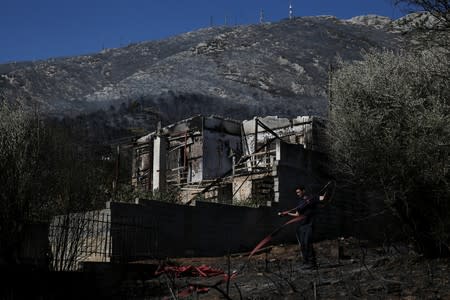 A firefighter arranges a hose outside a burned down house during a wildfire on Mount Hymettus, near Athens