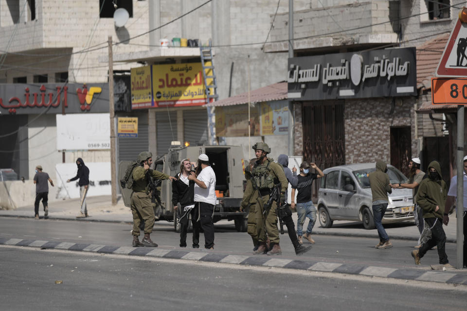 Israeli soldiers and Israeli settlers during clashes when the settlers attacked Palestinians in Huwara, near the West Bank town of Nablus, Thursday, Oct. 13, 2022. (AP Photo/Majdi Mohammed)