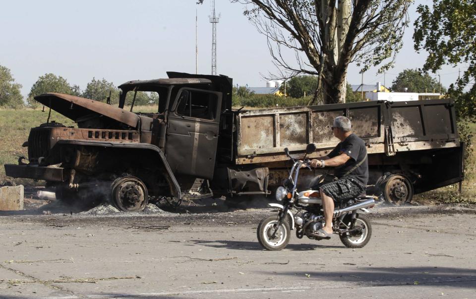 A local man rides a motorcycle past a truck burned by recent shelling on the outskirts of the southern coastal town of Mariupol September 7, 2014. Prolonged artillery fire was heard late on Saturday to the east of the port of Mariupol in eastern Ukraine, a Reuters reporter said, in what may be the first significant violation of a ceasefire declared little more than 24 hours earlier. REUTERS/Vasily Fedosenko (UKRAINE - Tags: CIVIL UNREST CONFLICT MILITARY POLITICS)