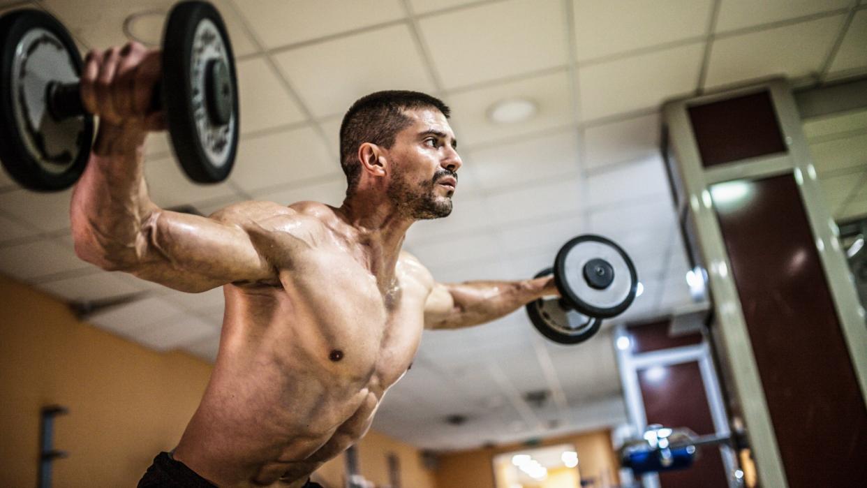  Man performing dumbbell lateral raises during upper body workout using two dumbbells. 