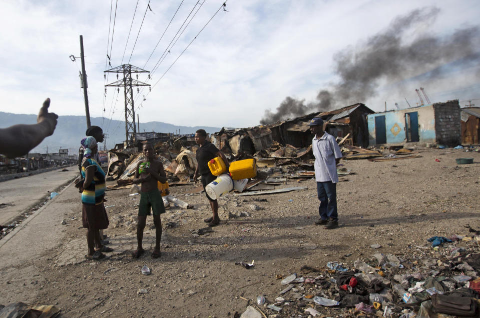 In this Nov. 21, 2018 photo, residents stand as they talk next to homes that were burned to the ground during a massacre in the La Saline slum of Port-au-Prince, Haiti. This is where a weeklong massacre began last year on Nov. 13, when men with guns and machetes broke into homes, killing at least 21 people and raping several women. (AP Photo/Dieu Nalio Chery)