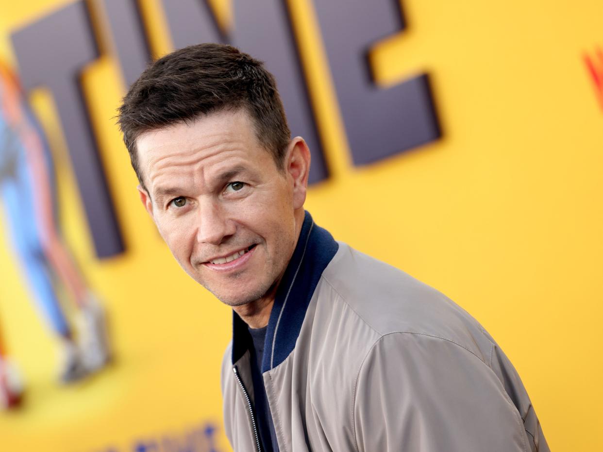 Mark Wahlberg in a grey jacket in front of a yellow backdrop