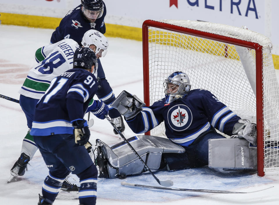 A stick-less Winnipeg Jets goaltender Laurent Brossoit (39) stops a shot as Vancouver Canucks' Sam Lafferty (18) looks for the puck and Cole Perfetti (91) and Neal Pionk (4) defend during the third period of an NHL hockey game Thursday, April 18, 2024, in Winnipeg, Manitoba. (John Woods/The Canadian Press via AP)