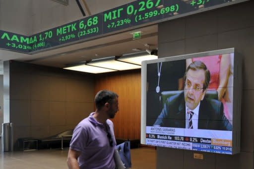 An employee at the Athens stock exchange walks past a television showing Antonis Samaras, the country's newly elected prime minister. Troubled eurozone nations agreed to act quickly to save Spain's banks, and to send international creditors to Greece for an update from the new government